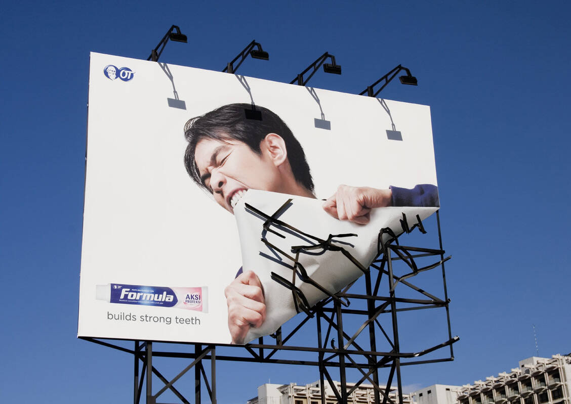 A billboard for Formula toothpaste in which a man appears to be ripping off a corner of the advertisement with his teeth.